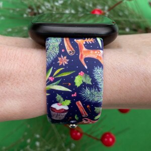 May include: A blue watch band with a Christmas-themed design. The band features a pattern of holly, cinnamon sticks, cupcakes, and reindeer on a dark blue background.
