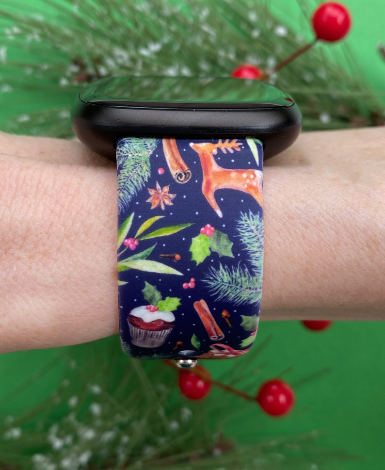 May include: A blue watch band with a Christmas-themed design. The band features a pattern of holly, cinnamon sticks, cupcakes, and reindeer on a dark blue background.