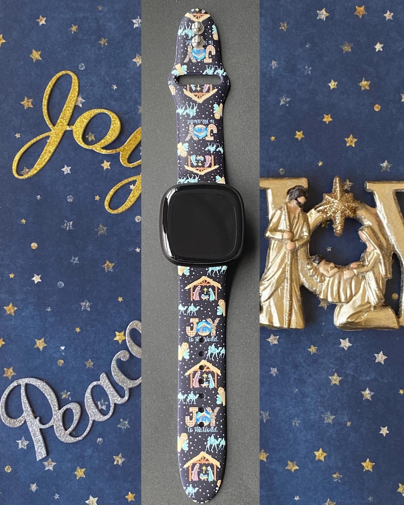 Pu&ograve; includere: Uno smartwatch nero con un cinturino fantasia raffigurante una scena della nativit&agrave;, cammelli e le parole "Joy to the World". Lo sfondo include le parole decorative dorate e argentate "Joy" e "Peace" e stelle dorate su sfondo blu scuro.