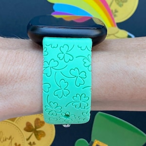 May include: A green smartwatch band with a clover pattern. The band is made of silicone and has a smooth finish.