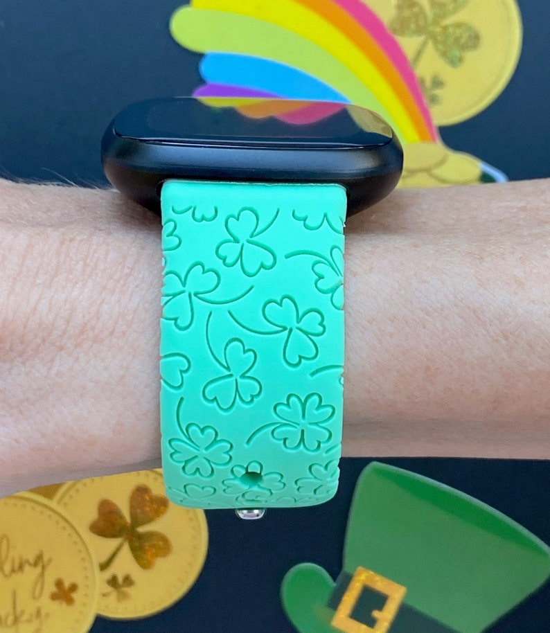 May include: A green smartwatch band with a clover pattern. The band is made of silicone and has a smooth finish.