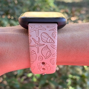 K&ouml;nnte beinhalten: Ein rosafarbenes Silikon-Armband mit Muschel- und Seestern-Design. Das Armband ist kompatibel mit Smartwatches.