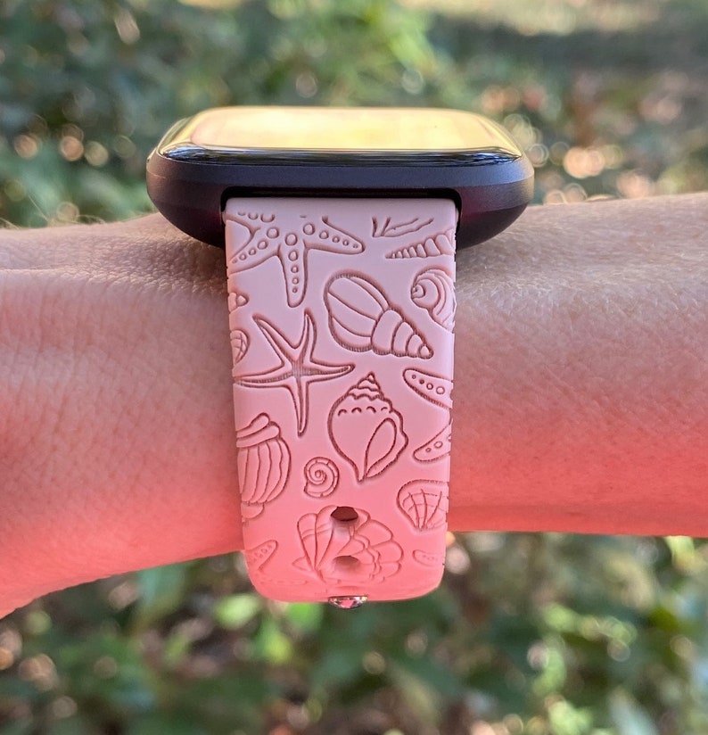 K&ouml;nnte beinhalten: Ein rosafarbenes Silikon-Armband mit Muschel- und Seestern-Design. Das Armband ist kompatibel mit Smartwatches.