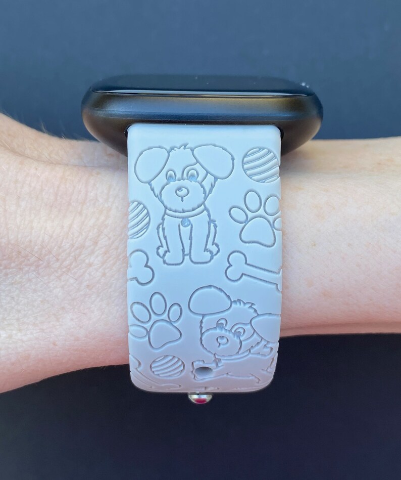 Puede incluir: Una correa de reloj de silicona gris con un patr&oacute;n de perro y hueso blanco. La correa est&aacute; dise&ntilde;ada para un reloj inteligente.