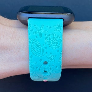 May include: A turquoise blue silicone watch band with a seashell and starfish pattern. The band is designed for a smartwatch.