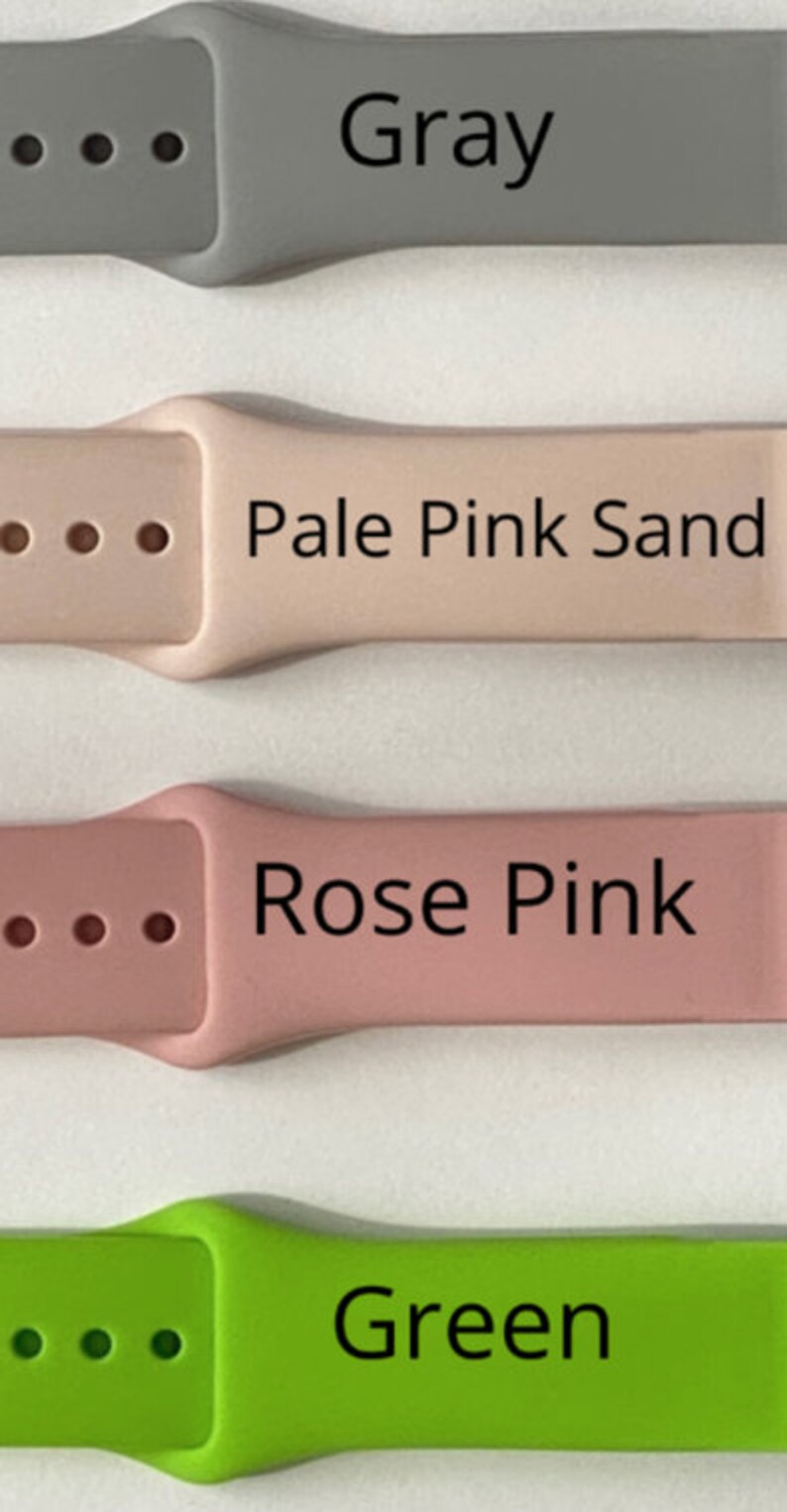 May include: A close-up of four watch straps in various colours: grey, pale pink sand, rose pink, and green. Each strap has its colour name printed in black. The straps are made of a flexible material and have adjustment holes.