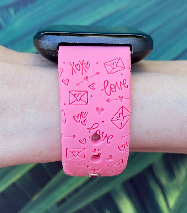 May include: Pink silicone watch band with a pattern of hearts, arrows, and envelopes with the words "XOXO" and "love" printed on it.