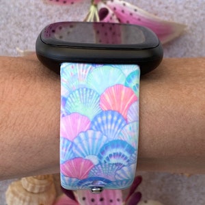 K&ouml;nnte beinhalten: Eine Smartwatch mit einem schwarzen Armband mit einem bunten Muschelmuster. Das Armband ist aus Silikon und hat einen wei&szlig;en Hintergrund mit blauen, rosa und gr&uuml;nen Muscheln.