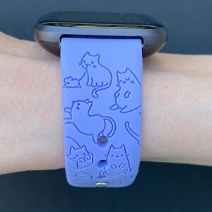 Pode incluir: Uma pulseira de rel&oacute;gio de silicone roxa com um padr&atilde;o de gatos e um rato. A pulseira &eacute; projetada para um smartwatch.