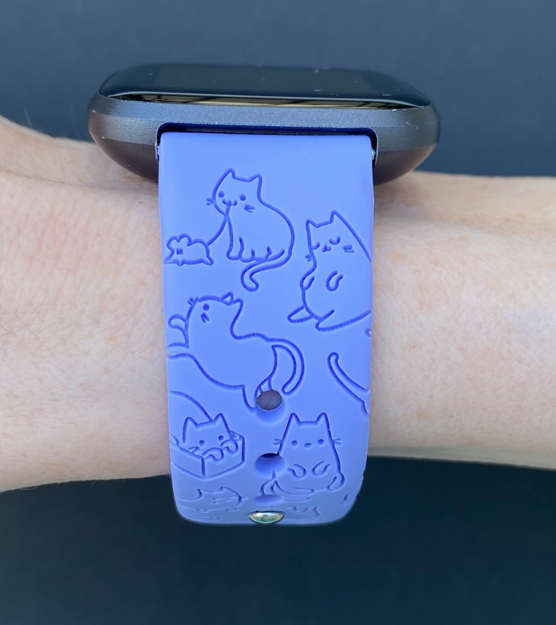 Pode incluir: Uma pulseira de rel&oacute;gio de silicone roxa com um padr&atilde;o de gatos e um rato. A pulseira &eacute; projetada para um smartwatch.