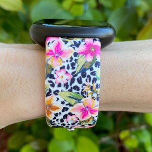 May include: A black smartwatch with a floral and leopard print silicone strap. The strap features pink, white, and yellow flowers on a black and white leopard print background.