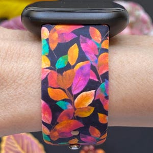 Pu&ograve; includere: Uno smartwatch nero con un cinturino colorato con un motivo a foglie nei toni dell'arancione, rosa, viola e verde. Il cinturino &egrave; attaccato a un polso, mostrando il design vibrante su uno sfondo scuro. Il cinturino &egrave; largo circa 2,5 cm.