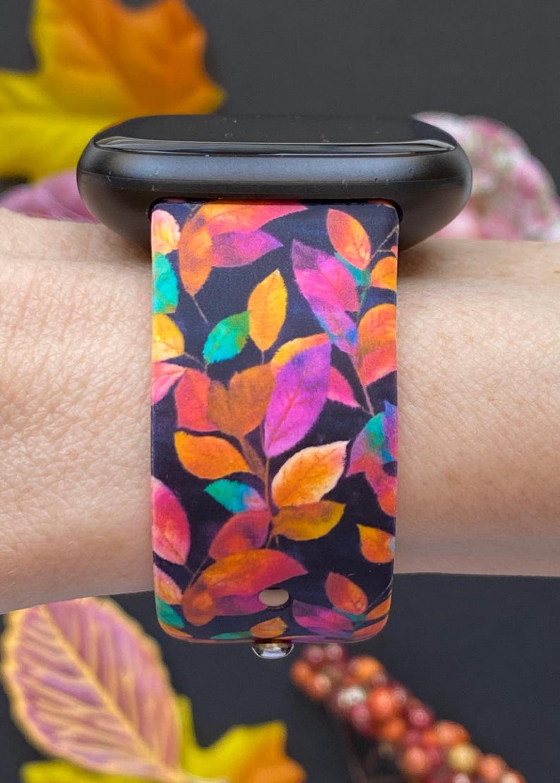 Pu&ograve; includere: Uno smartwatch nero con un cinturino colorato con un motivo a foglie nei toni dell'arancione, rosa, viola e verde. Il cinturino &egrave; attaccato a un polso, mostrando il design vibrante su uno sfondo scuro. Il cinturino &egrave; largo circa 2,5 cm.