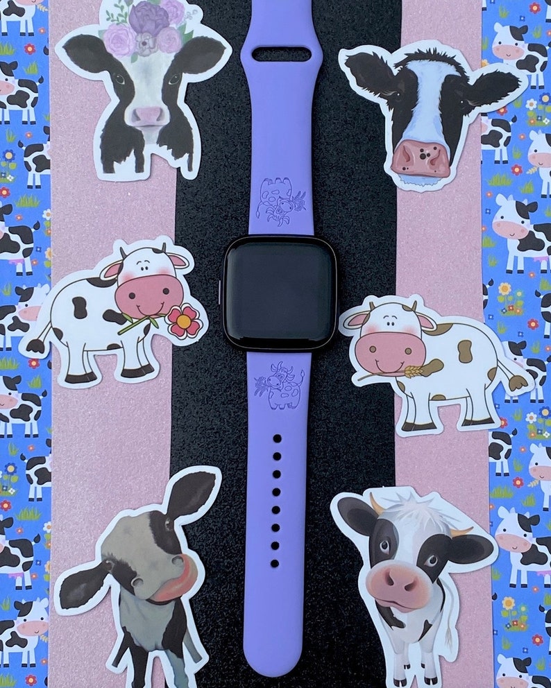 Peut inclure: Un bracelet de montre Apple en silicone violet avec un motif de vache. Le bracelet a un cadran noir et est entour&eacute; d'autocollants de vache.
