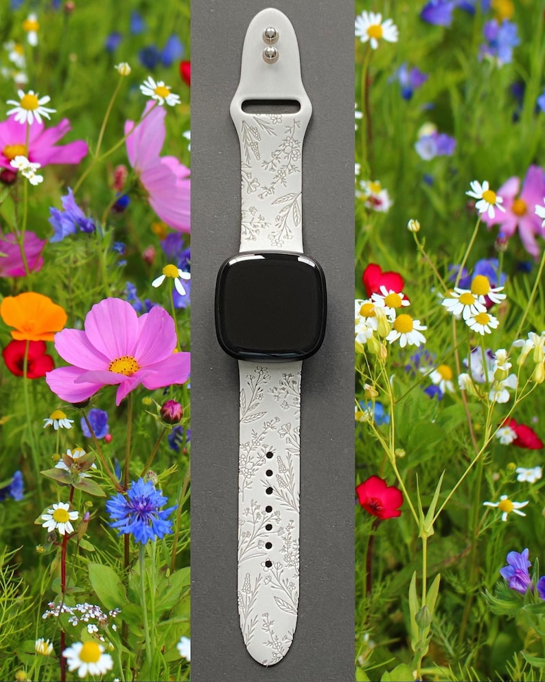 May include: White silicone watch band with a floral pattern. The band is shown on a black watch face and is surrounded by a field of wildflowers.