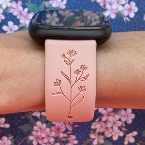 May include: A pink silicone watch band with a delicate floral design. The band is compatible with smartwatches.