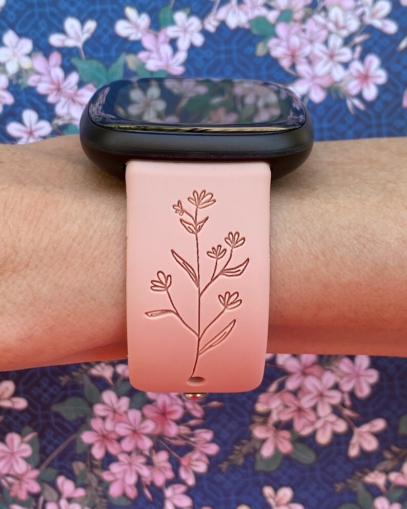 May include: A pink silicone watch band with a delicate floral design. The band is compatible with smartwatches.