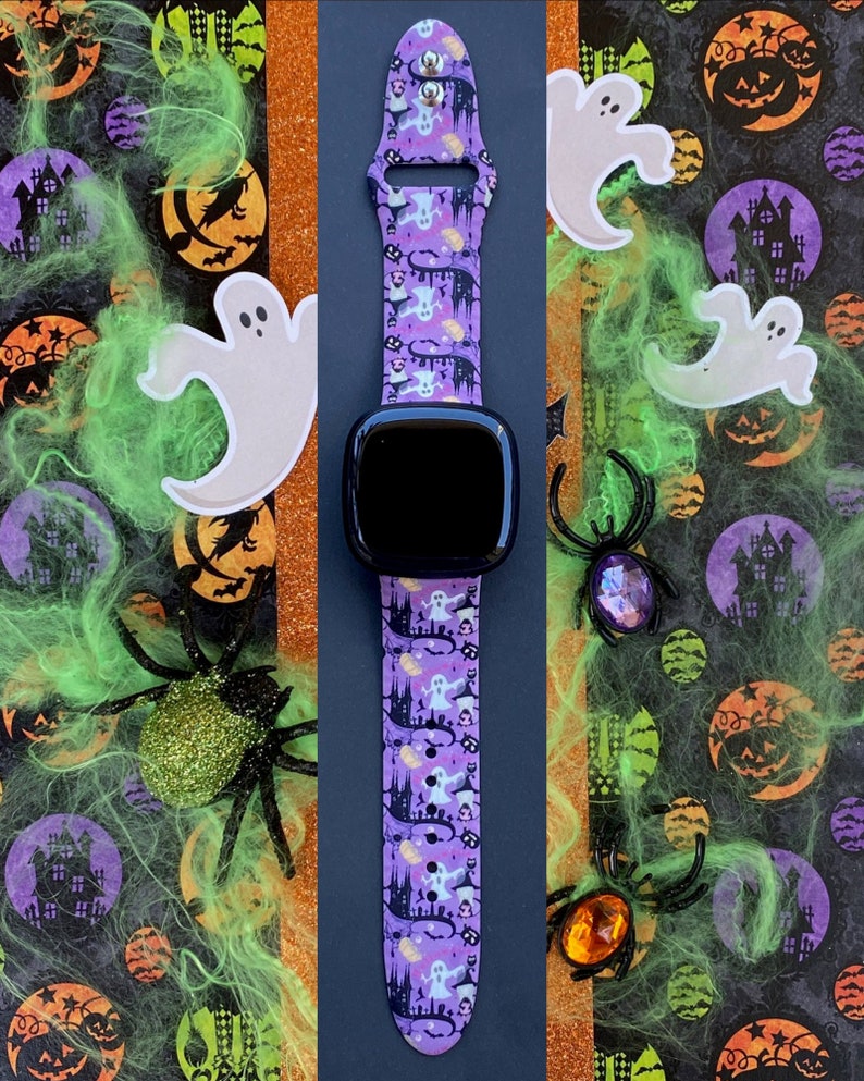 May include: A purple and black watch band with a Halloween theme. The band features ghosts, pumpkins, and haunted houses. The watch face is black and the band is made of silicone.