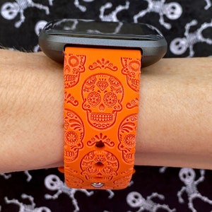 K&ouml;nnte beinhalten: Orangefarbenes Silikon-Armband mit Totenkopf-Design. Das Armband wird am Handgelenk getragen.