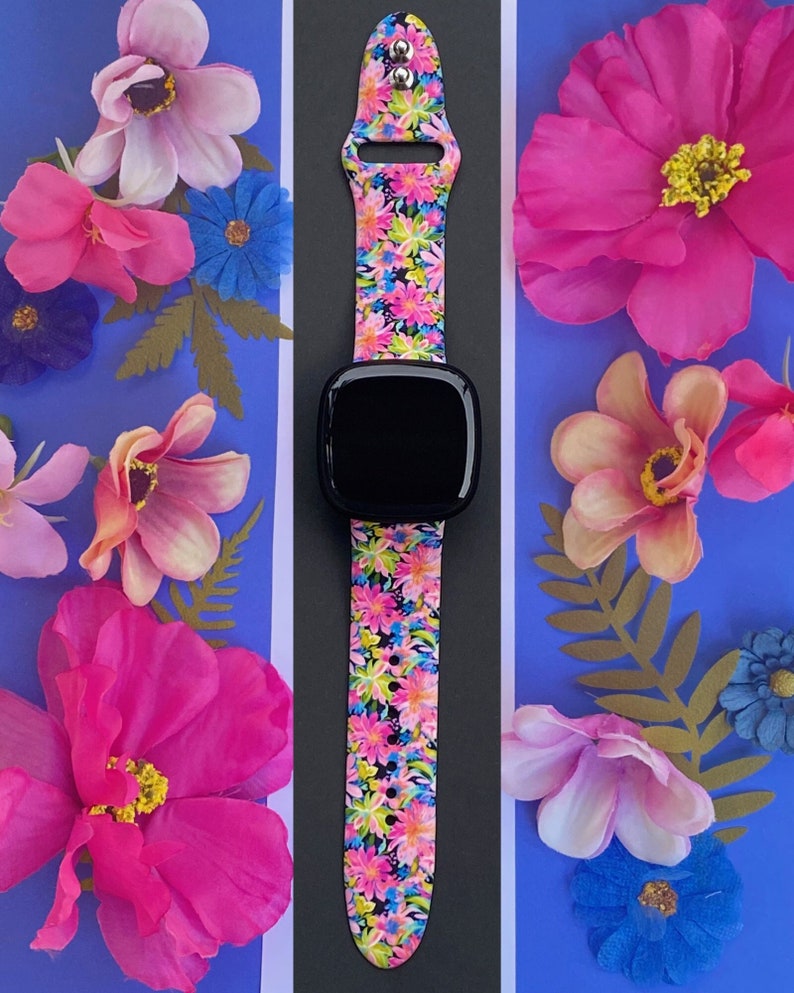 May include: A black smartwatch with a bright pink, yellow, and green floral patterned band. The band has small silver studs on the top.