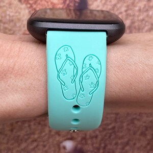 May include: A turquoise blue silicone watch band with a design of two flip flops with white flowers on them.