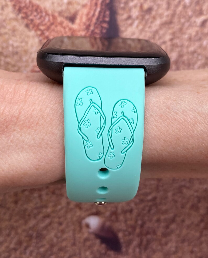 May include: A turquoise blue silicone watch band with a design of two flip flops with white flowers on them.