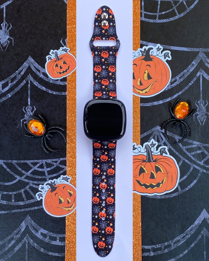 K&ouml;nnte beinhalten: Ein schwarz-wei&szlig;es Armband mit Halloween-Motiv. Das Armband zeigt ein sich wiederholendes Muster aus orangefarbenen K&uuml;rbissen mit Jack-o'-Lantern-Gesichtern, Candy Corn und Spinnweben. Das Armband ist auf wei&szlig;em Hintergrund abgebildet.