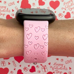 May include: A pink silicone watch strap with a heart pattern. The strap is on a person's wrist.