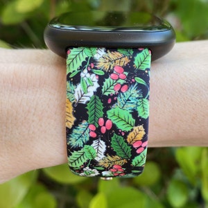 May include: A black smartwatch with a green, red and gold floral patterned band. The band has a repeating pattern of leaves, berries and flowers.