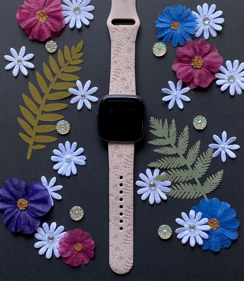 May include: A pink smartwatch band with a floral pattern. The band is made of silicone and has a smooth finish. The band is compatible with most smartwatches.