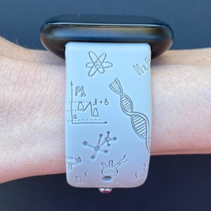 Pu&ograve; includere: Un cinturino per orologio in silicone bianco con un quadrante nero. Il cinturino ha un tema scientifico con disegni di una catena di DNA, un atomo, una beuta e un grafico. Il testo "H2O" &egrave; visibile sul cinturino.