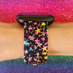 May include: A black smartwatch with a colorful star pattern band. The band has a variety of colors including pink, blue, yellow, and green.
