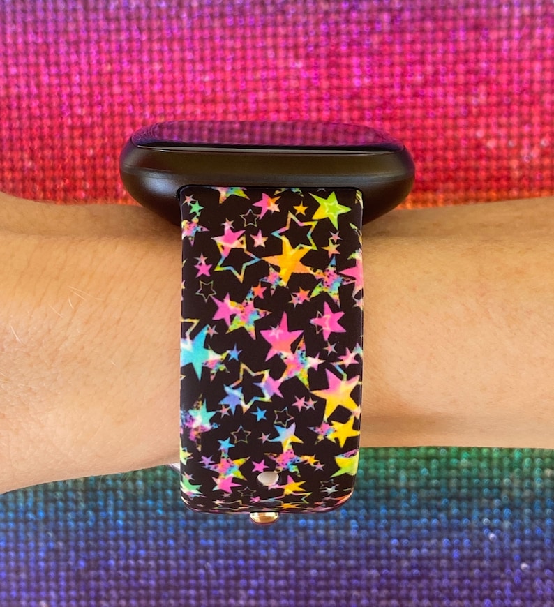 May include: A black smartwatch with a colorful star pattern band. The band has a variety of colors including pink, blue, yellow, and green.