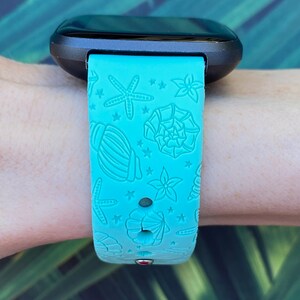 May include: A turquoise blue silicone watch band with a seashell and starfish design. The band is compatible with a smartwatch.