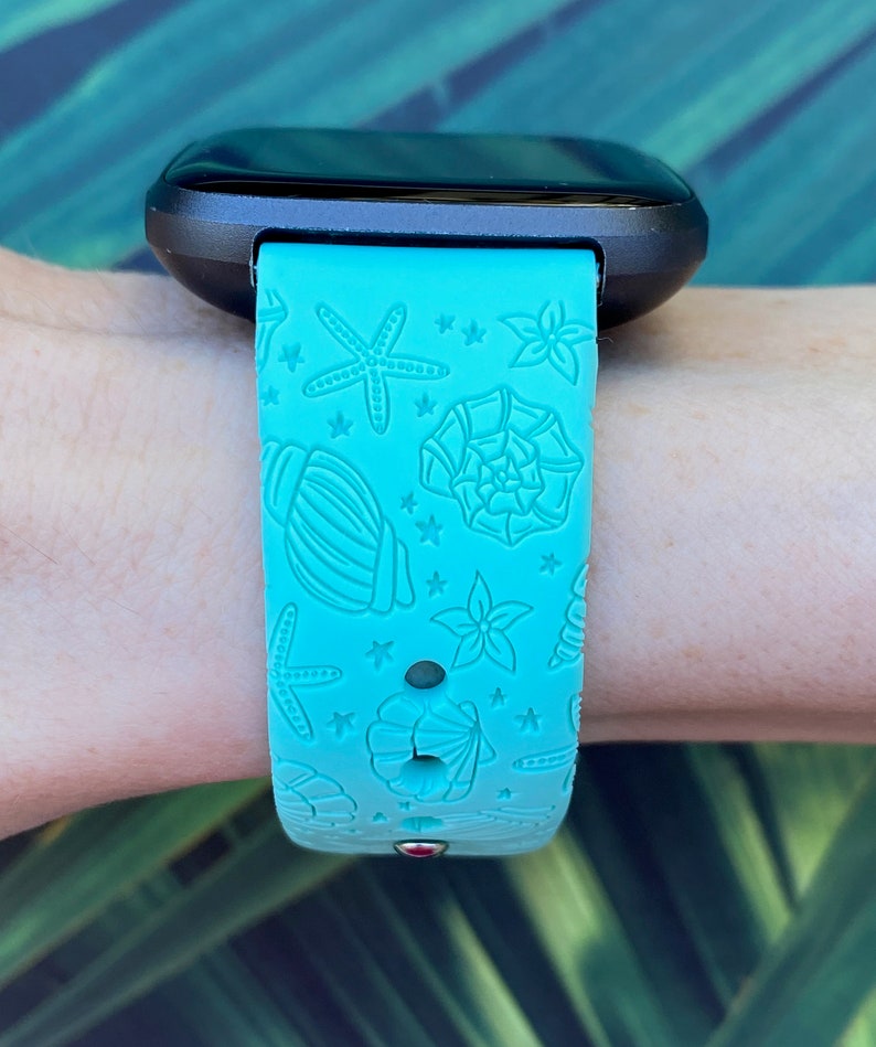 May include: A turquoise blue silicone watch band with a seashell and starfish design. The band is compatible with a smartwatch.