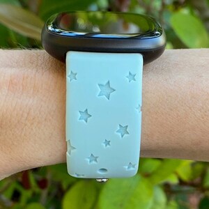 May include: A light blue silicone watch band with a star pattern. The band is on a person's wrist.
