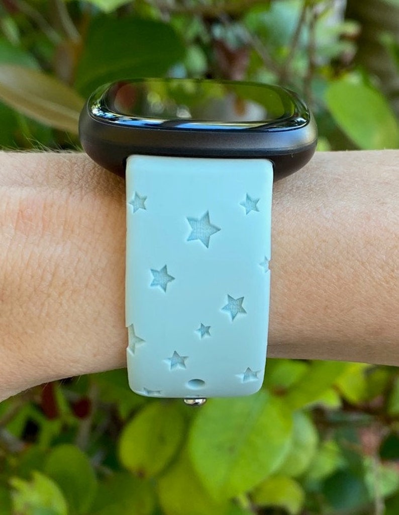 May include: A light blue silicone watch band with a star pattern. The band is on a person's wrist.