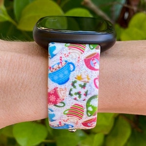 Puede incluir: Una banda de reloj blanca con un patr&oacute;n colorido de tazas llenas de chocolate caliente y bastones de caramelo. La banda est&aacute; hecha de silicona y tiene un tema festivo navide&ntilde;o.
