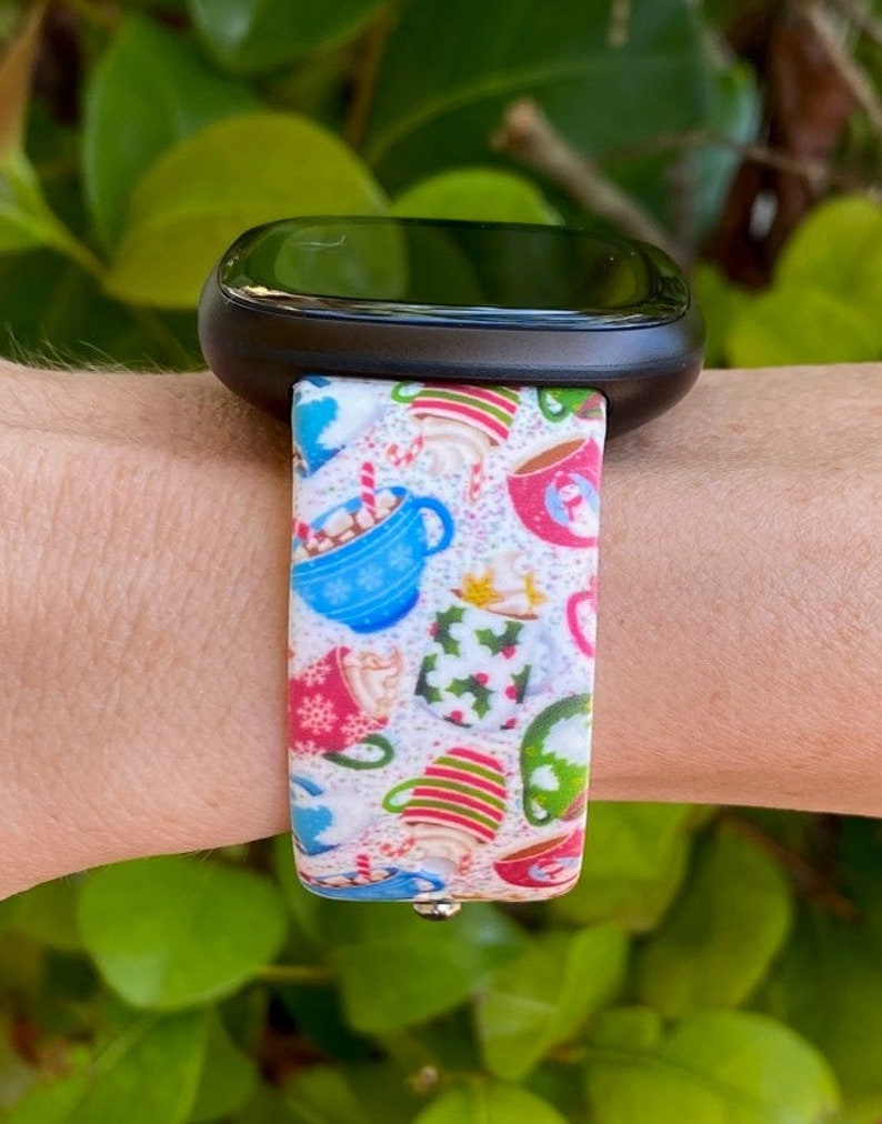 Puede incluir: Una banda de reloj blanca con un patr&oacute;n colorido de tazas llenas de chocolate caliente y bastones de caramelo. La banda est&aacute; hecha de silicona y tiene un tema festivo navide&ntilde;o.