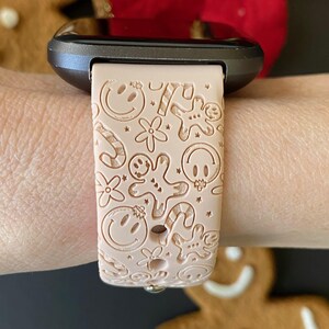 May include: A pink silicone watch band with a festive design featuring gingerbread men, candy canes, and smiley faces.