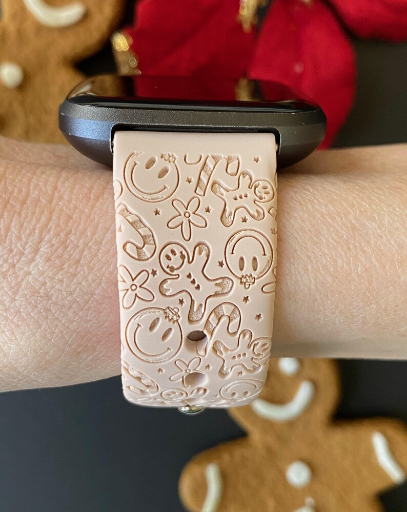 May include: A pink silicone watch band with a festive design featuring gingerbread men, candy canes, and smiley faces.
