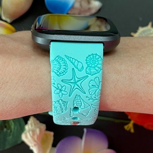 May include: A turquoise blue watch band with a seashell and starfish design. The band is made of silicone and has a black watch face.