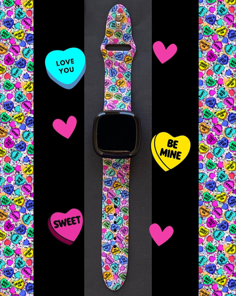 Puede incluir: Un reloj inteligente negro con una banda estampada de corazones de caramelo coloridos. La banda presenta varios corazones de caramelo con frases como "Be Mine", "Love You" y "Sweet".