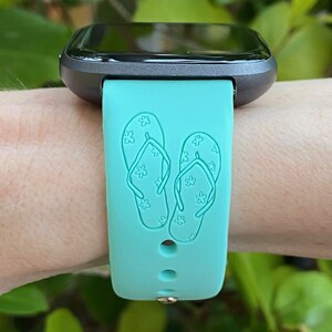 May include: A turquoise blue smartwatch band with a design of two flip flops with white flowers on them.