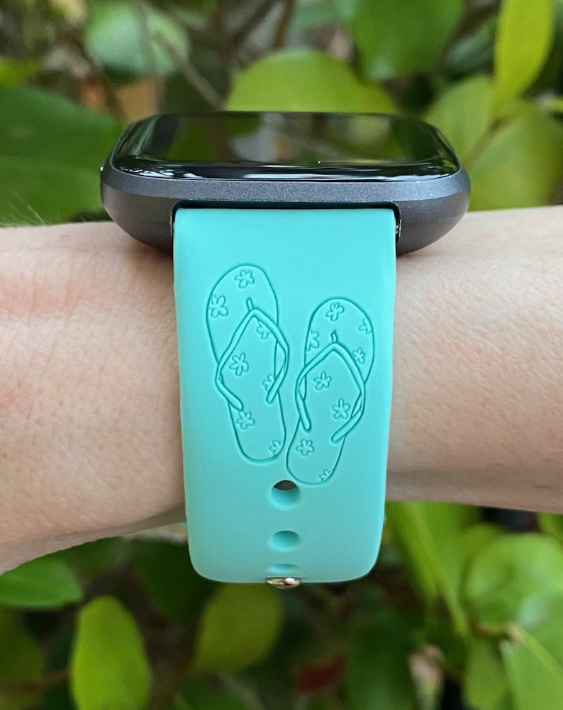 May include: A turquoise blue smartwatch band with a design of two flip flops with white flowers on them.