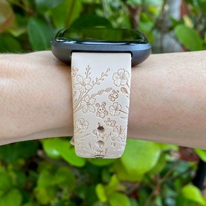 May include: A white watch band with a floral and bee design. The band is made of silicone and has a black watch face.