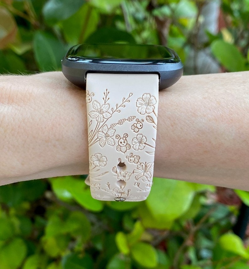 May include: A white watch band with a floral and bee design. The band is made of silicone and has a black watch face.