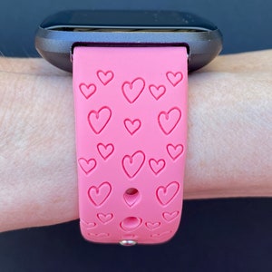 May include: A pink silicone watch strap with a heart pattern. The strap is designed for a smartwatch and has a silver buckle.