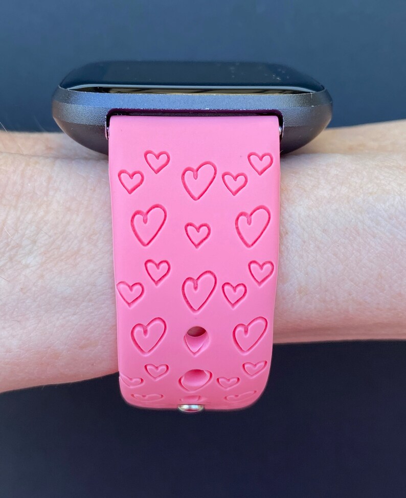 May include: A pink silicone watch strap with a heart pattern. The strap is designed for a smartwatch and has a silver buckle.