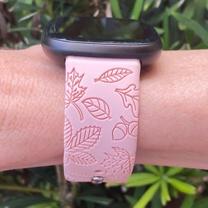 May include: A pink silicone watch band with a leaf and acorn design. The band is compatible with a smartwatch.